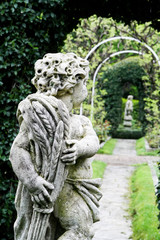 Fototapeta premium Statue of the boy in the garden. In the background is another statue