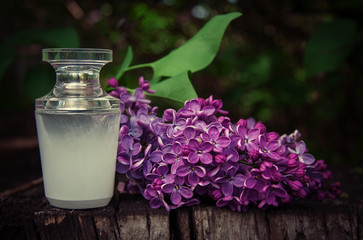 Obraz na płótnie Canvas Perfume bottle with a sprig of lilac on a wooden background