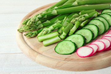 fresh asparagus c chopped radishes and cucumber on wooden cutting Board on white wooden background