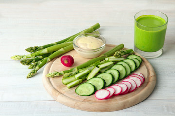 fresh asparagus c chopped radishes and cucumber on wooden cutting Board with sauce on white wooden background with a glass of juice of asparagus