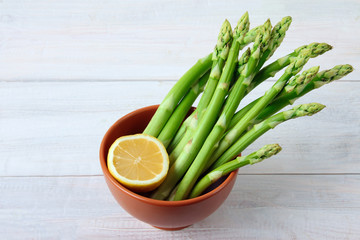 fresh asparagus cut lemon in brown bowl on white wooden background