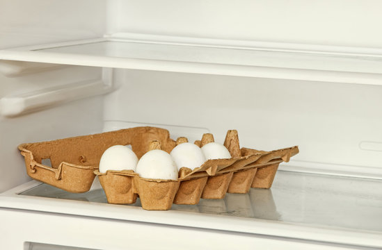 Eggs in a paper box on refrigerator shelf.