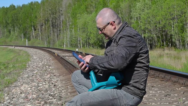 Disabled man with crutches sitting on railway and using tablet PC
