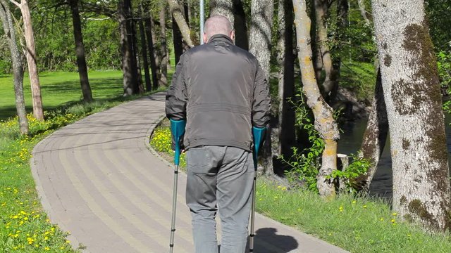 Disabled man with crutches walking away on path
