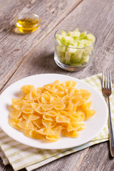 Farfalle on a white plate on wooden background, top view