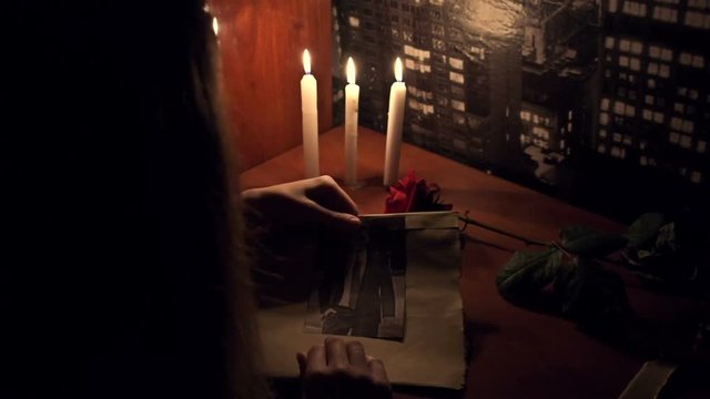 The girl in the candlelight looking at a photo of a young man
