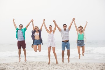 Obraz premium Portrait of friends holding hands and jumping on the beach