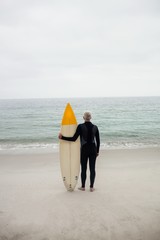 Rear view of senior man in wetsuit holding a surfboard