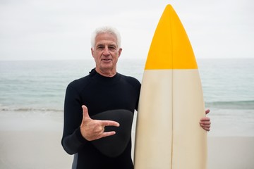 Senior man with surfboard gesturing hand sign at beach