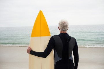 Rear view of senior man in wetsuit holding a surfboard
