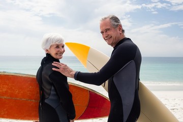 Senior couple in wetsuit holding surfboard on beach 