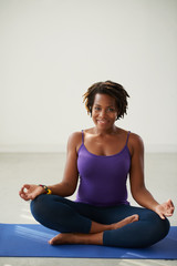Fototapeta premium Smiling African-American woman sitting on yoga mat in lotus position