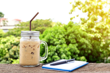 Ice coffee cup with handle with a notebook and pen on the old wooden floor.