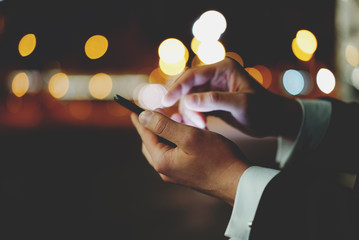 Close-up of male hands using modern smartphone at night outside, bokeh light, professional businessman using his cellphone at night