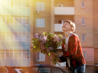 Happy girl with big bouquet of flowers laughing happily in the sun on a background of a new, multi-storey building - new building. Concept - happiness, joy, buying apartments, new housing
