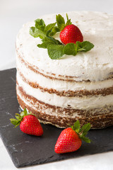Delicious white cream icing cake with strawberry on the black board. Naked cake with cream, decorated with strawberries and mint.
