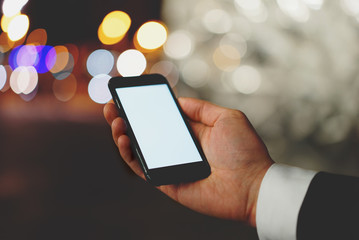 Male employer using modern smartphone with blank screen for your text message, professional businessman showing his cellphone with empty display at night city, blurred background, bokeh light