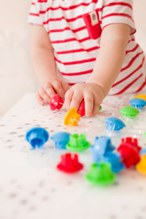 Closeup of child's hand taking bright mosaic parts. Playing and learning colors at home. Toddler boy in a striped shirt playing with colorful constructor details. Activities with children
