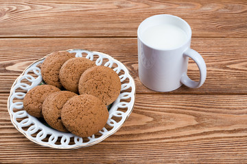 Oatmeal cookies on a plate and cup of milk on a wooden background 
