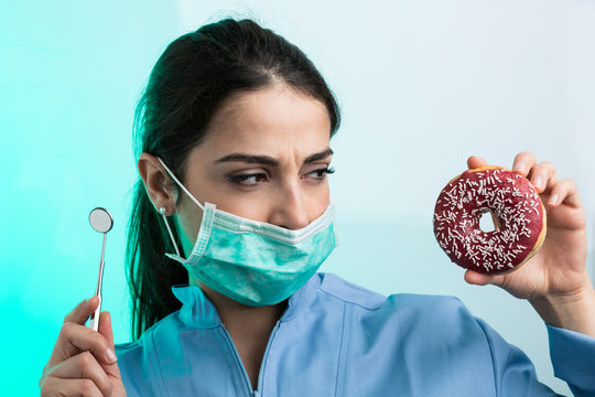 giovane dentista guarda con aria di sfida una ciambella togliendosi la mascherina - sfondo verde