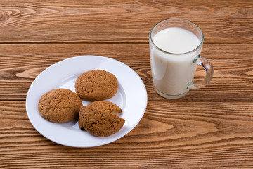 Oatmeal cookies on a plate and cup of milk on a wooden background 