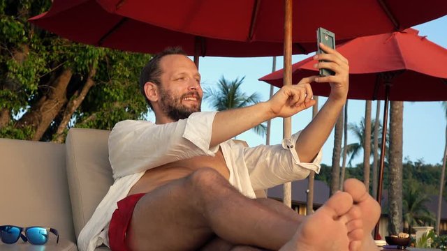 Young man on sunbed taking selfie photo with cellphone 
