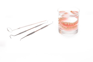 dentures in glass of water and tools on white background