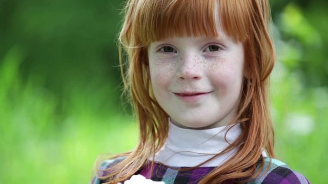 Close up little ginger girl's face  smiling in the park, green background outdoors