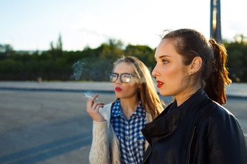 Two beautiful young girls to smoke while waiting outdoors