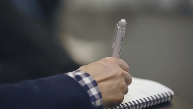 Close up, over the shoulder shot of a business man holding a pen, thinking and making notes in notebook during business meeting or conference or training. 