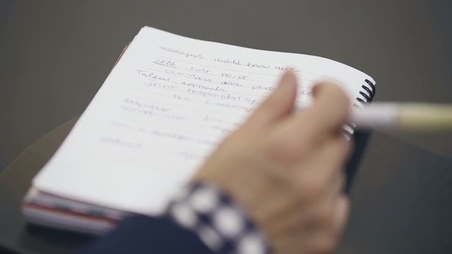 Close up, over the shoulder shot of a business man holding a pen, thinking and making notes in notebook during business meeting or conference or training. 