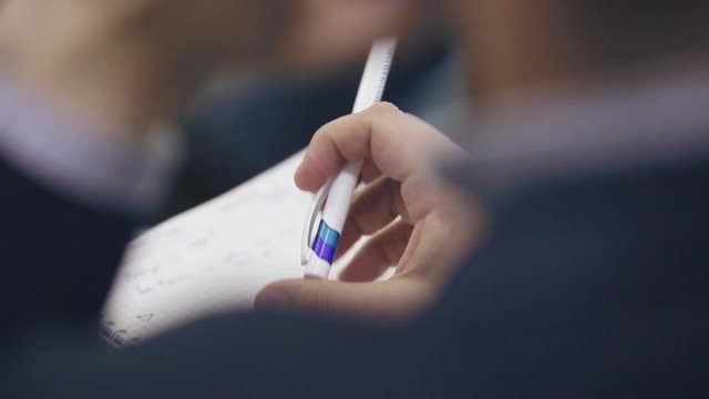 Close up, over the shoulder shot of a business man holding a pen, thinking and making notes in notebook during business meeting or conference or training. 