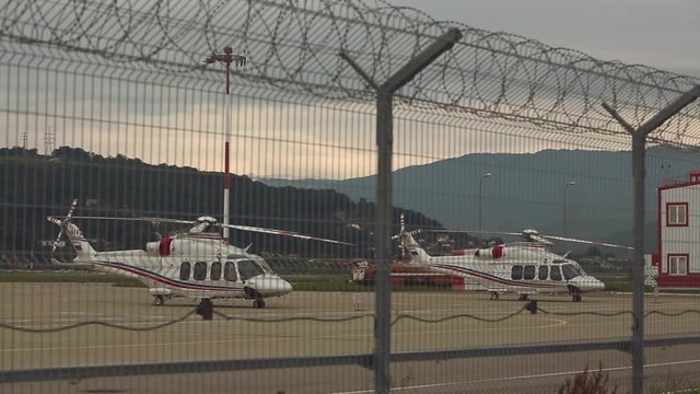 Two helicopters standing on  helicopter pad or platform against background with sunset, mountain covered with forests and metal fence or barbed wire in the foreground.Rack focus, wide shot. 
