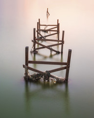 An old, unused wooden fishing pier on very calm sea during dusk.