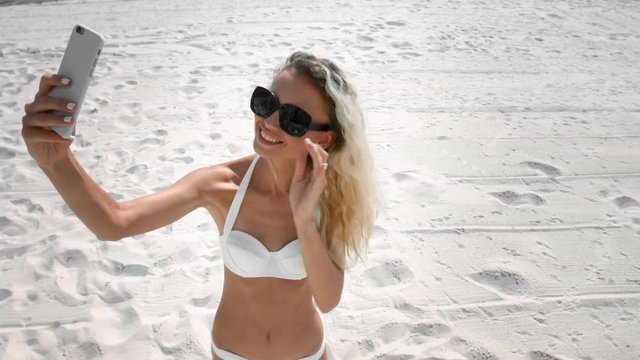 Slim tan girl in white bikini make selfie on a beach