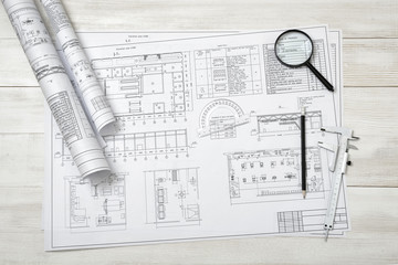 Rolls of drawing sketches, magnifier, ruler and protractor are on wooden surface.