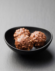 Chocolate candies, truffle in ceramic black bowl on grey slate background Copy space.