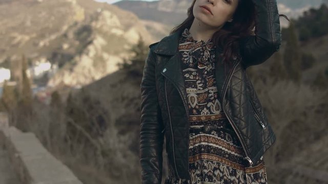 Beautiful girl in a dress and leather jacket posing while standing on the parapet