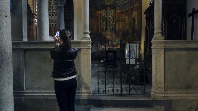 Young woman taking photo with cellphone 
of catholic temple 