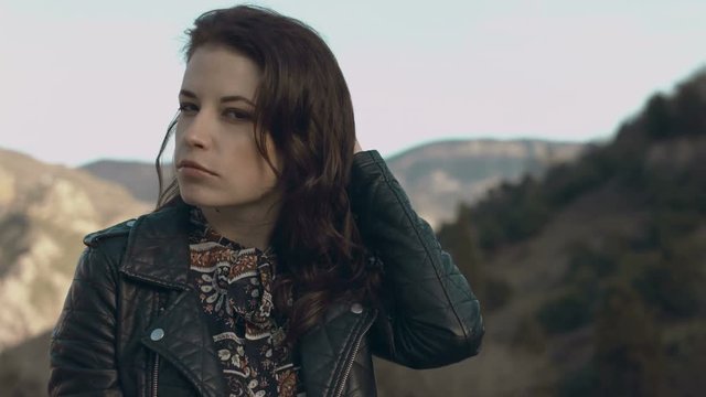 Beautiful girl in a dress and leather jacket posing while standing on the parapet