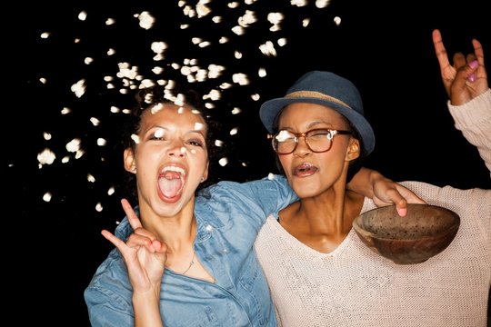 Young women throwing popcorn from bowl looking at camera doing rock sign
