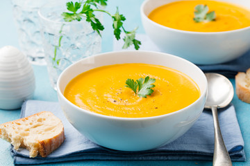 Pumpkin and carrot soup with cream and parsley on blue stone background.