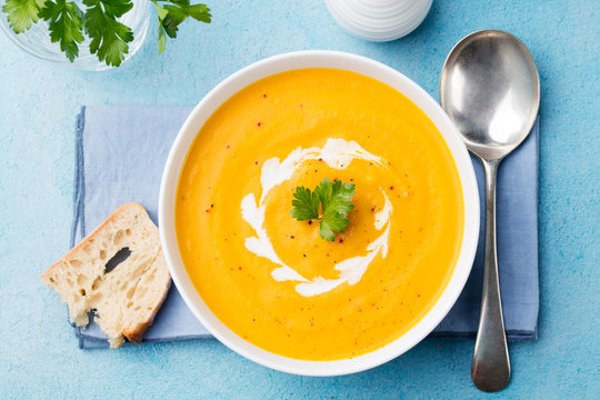 Pumpkin and carrot soup with cream and parsley on blue stone background Top view.