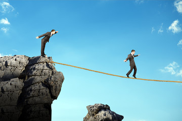Businessman walking on rope above gap