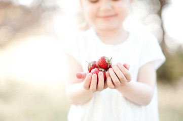Cute kid girl holding strawberry outdoors. Selective focus.