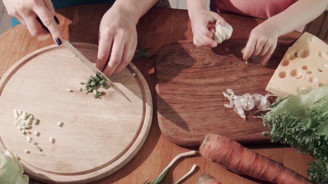 Close-up of unrecognizable woman and girl preparing healthy food cutting onion and garlic on the wooden chopping board. Shot from above