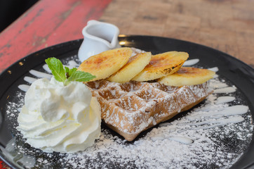 Chocolate waffle serve with banana and whip cream in black plate