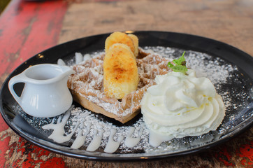 Chocolate waffle serve with banana and whip cream in black plate