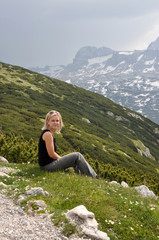 Naklejka na ściany i meble Blonde girl sitting on the grass and looking at the mountains, D