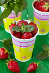Ripe sweet strawberry and mint leaves on a green painted wooden table